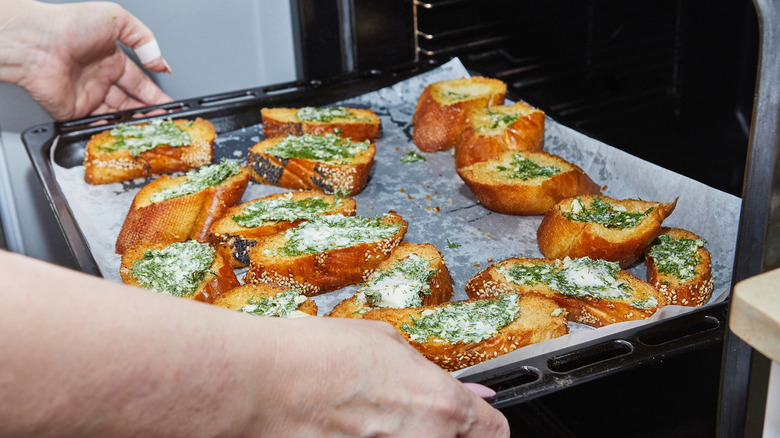 Hands pulling a tray of garlic bread out of oven