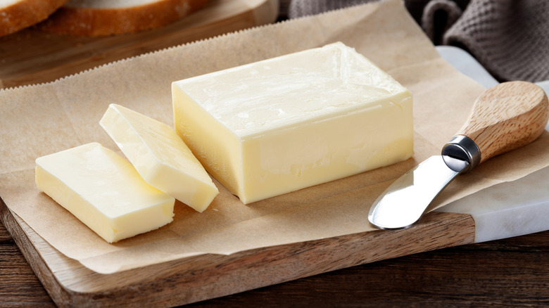 Block and slices of butter on cutting board with a butter knife