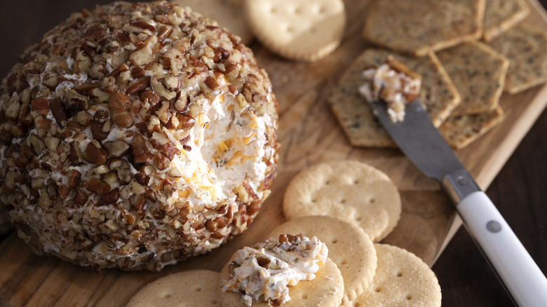 Old-fashioned cheese ball coated in nuts on a wooden platter with crackers