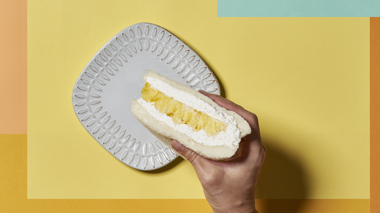 Hand holding a retro pineapple sandwich against a white plate and colorful background