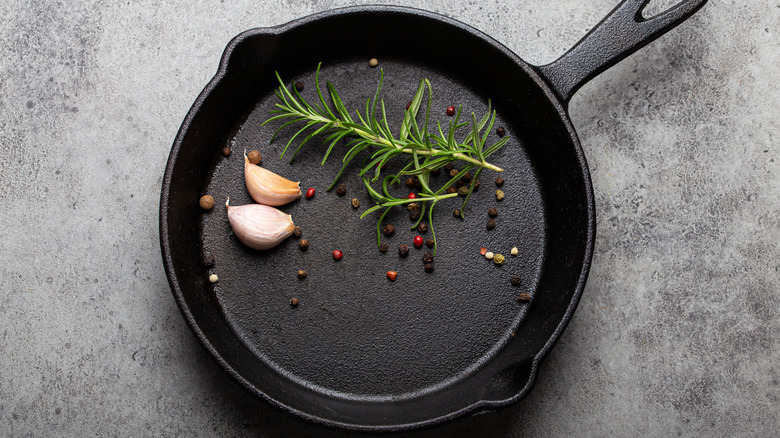 Overhead shot of cast iron skillet containing garlic, rosemary, and peppercorns