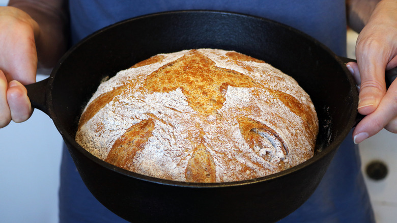 Hands holding Dutch oven filled with a freshly baked bread loaf