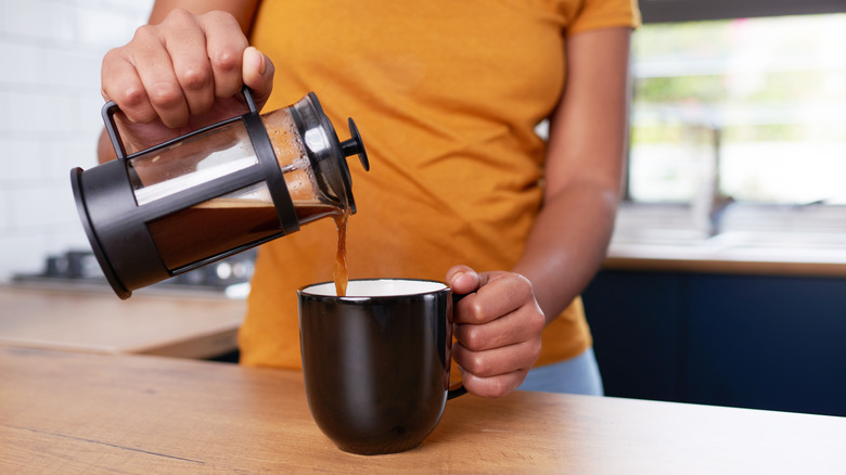 Person pouring cup of coffee from a French press