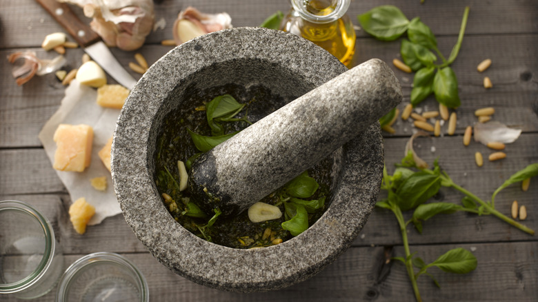 Mortar and pestle filled with and surrounded by pesto ingredients