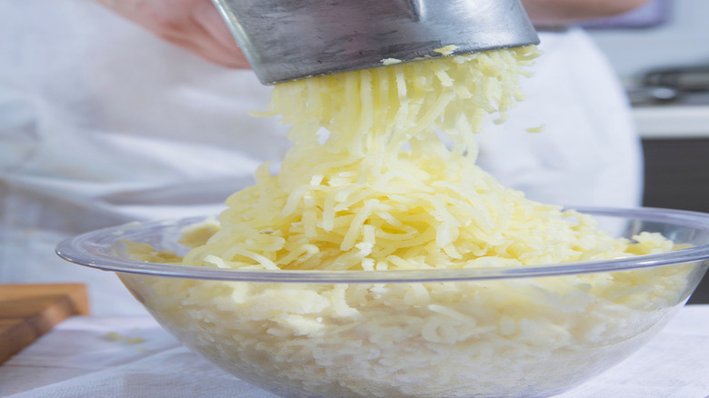 Closeup of potatoes being pushed through a ricer