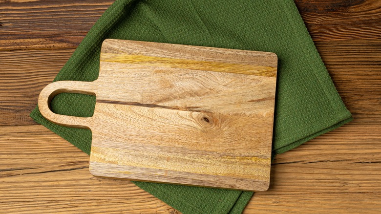 Empty wooden cutting board on counter with a green towel under it