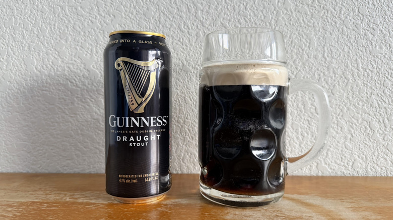 Guinness Draught Stout can beside a mostly full glass