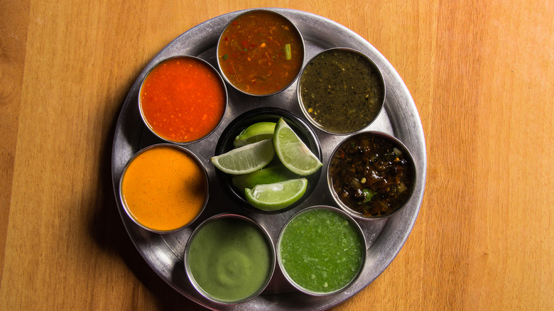 A selection of different Mexican salsas in ramekins on a metal platter surrounding a ramekin of freshly cut lime wedges