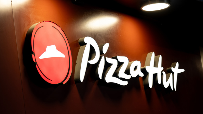 A red and white Pizza Hut sign with a light above it.