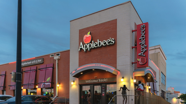 The outside of an Applebee's building at night with people in front of it.