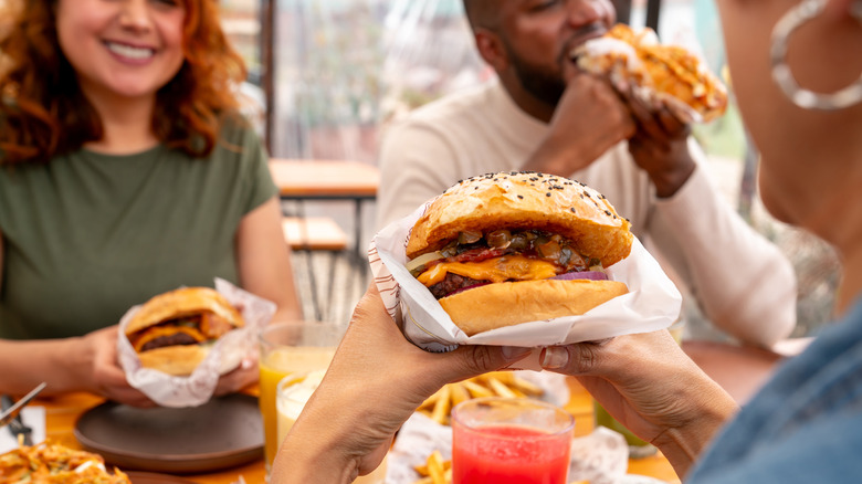 A group of people sitting at a table and eating burgers and fries.