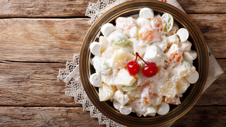 Top view of a bowl of ambrosia salad with oranges, pineapples, and maraschino cherries on a table