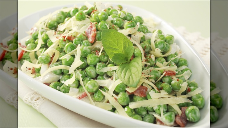 Pea salad with bacon and cheddar cheese shavings in an elegant white bowl
