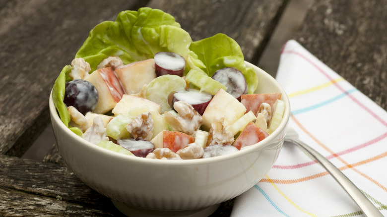A bowl of Waldorf salad on a table, with a folded napkin and fork beside it