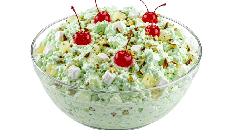 A bowl of Watergate salad topped with maraschino cherries against a white background