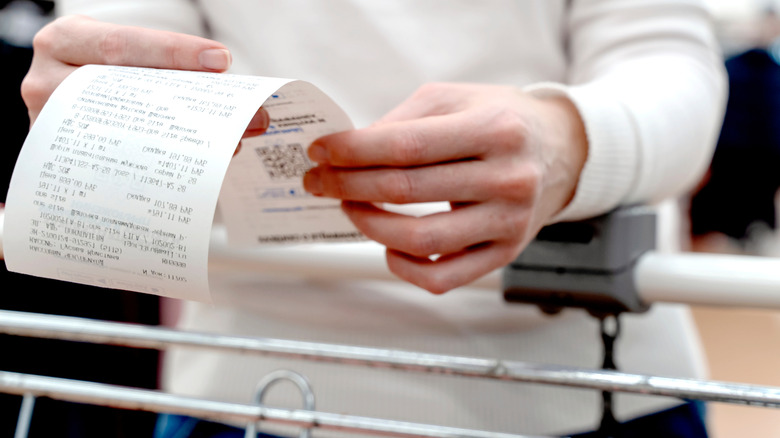 Hands holding receipt over shopping cart
