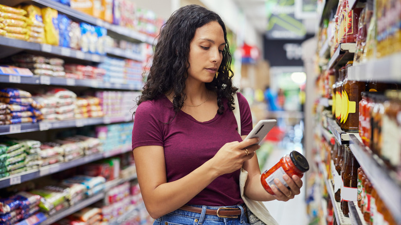 Woman scanning jar of sauce in grocery store aisle with phone