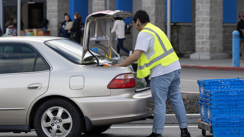 Grocery store working loading bags into the trunk of a customer's car for curbside pickup