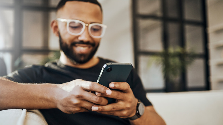 Man smiles while using smartphone on sofa
