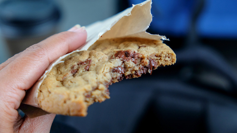 A hand holding a bitten chocolate chip cookie.