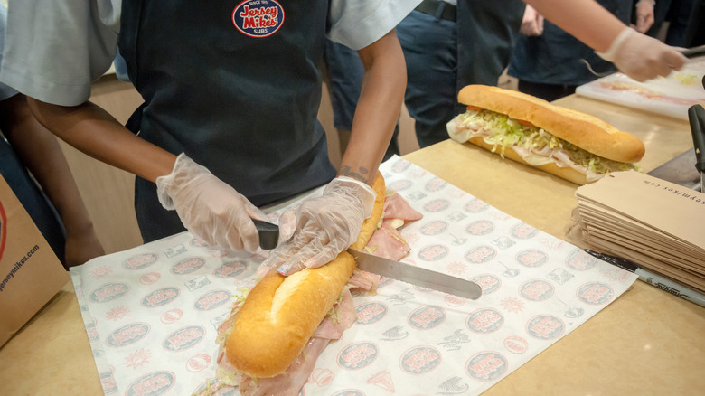 A Jersey Mike's employee cutting a sandwich.