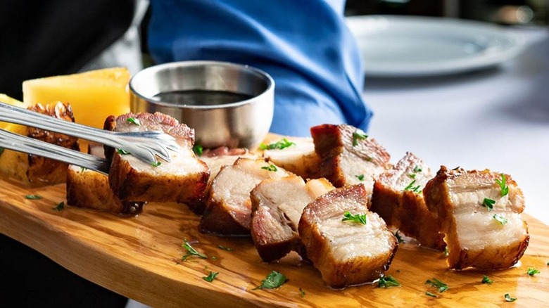 A guest using the required tongs to pick up a piece of pork belly