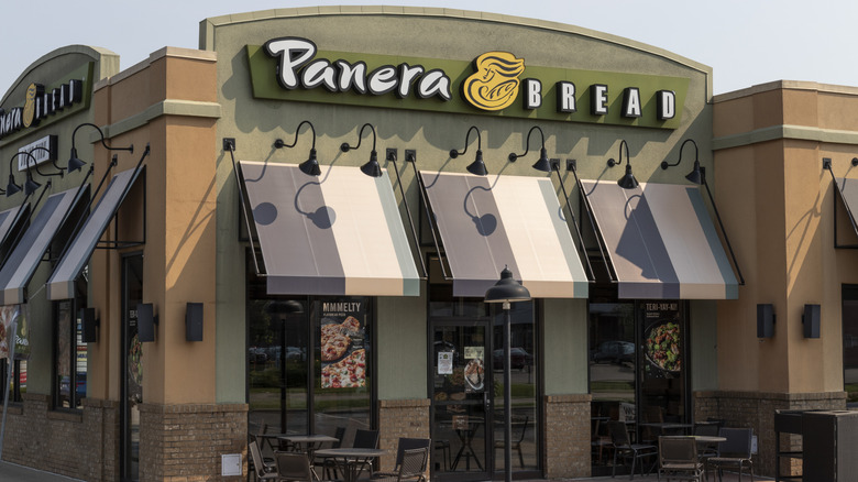 exterior shot of a Panera Bread from parking lot, showing restaurant awnings and patio tables