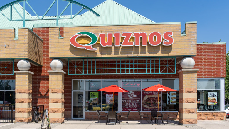 exterior of a Quiznos restaurant with patio seating under umbrellas