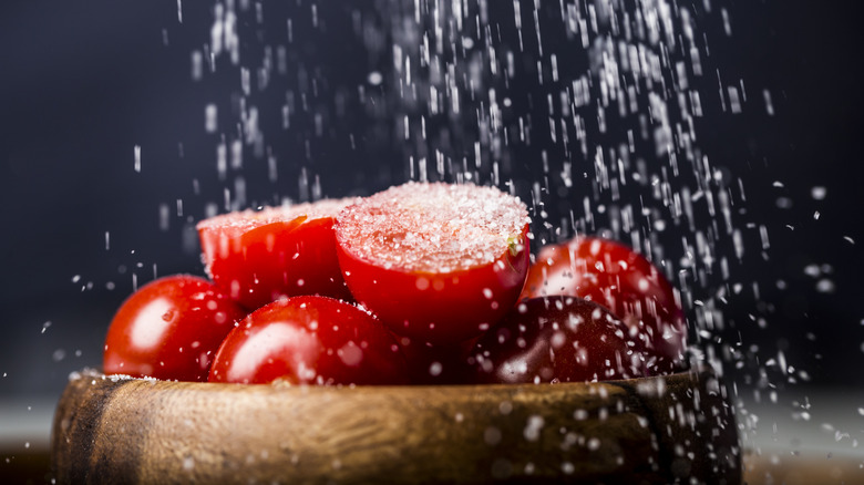 Salt being sprinkled over tomatoes in a wooden bowl