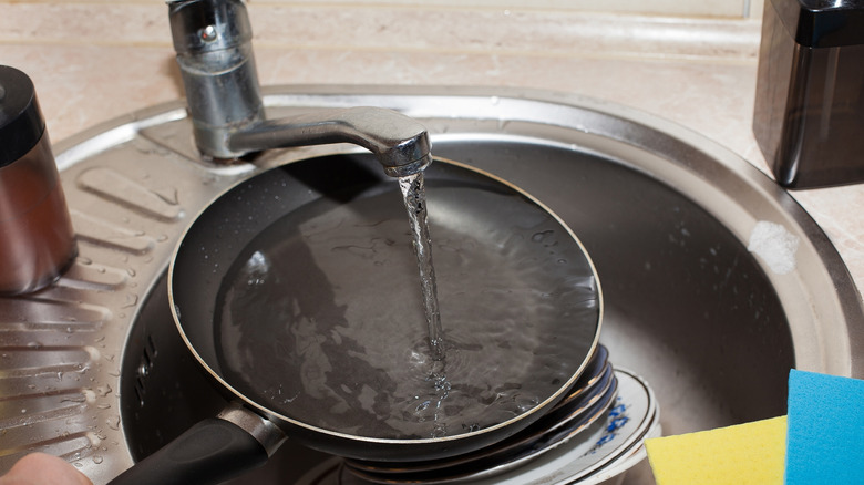 A frying pan being run under water in a sink