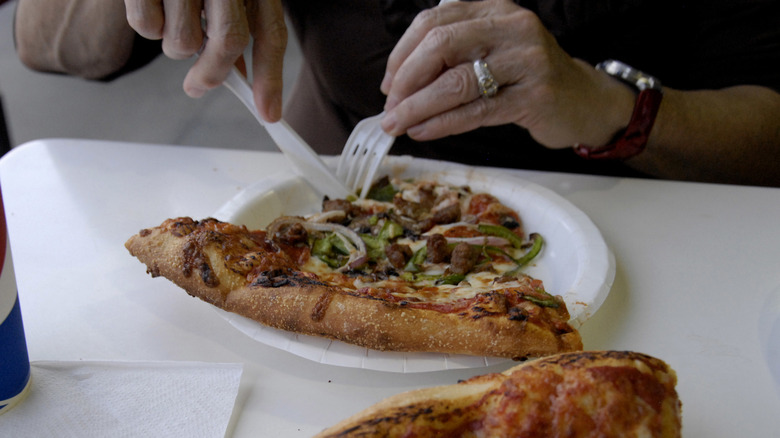 someone cutting into a slice of Costco's combo pizza