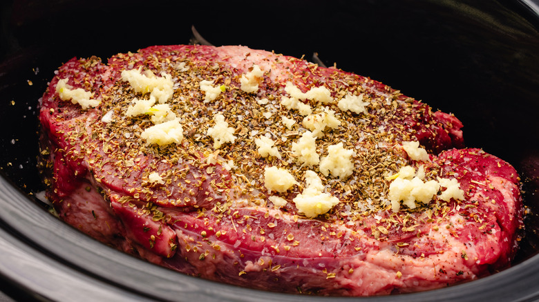 Raw chuck roast seasoned with raw garlic and herbs