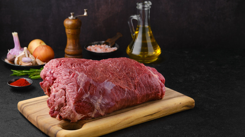 Chuck roast on a cutting board next to herbs and oil