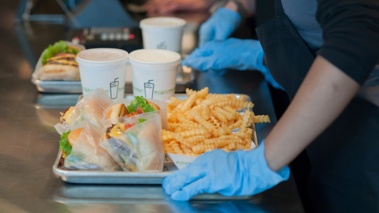 Gloved Shake Shack employees wait for customers to retrieve their trays of food.