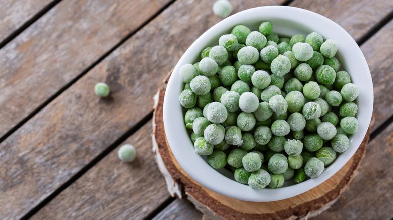 Bowl of frozen peas on wooden table
