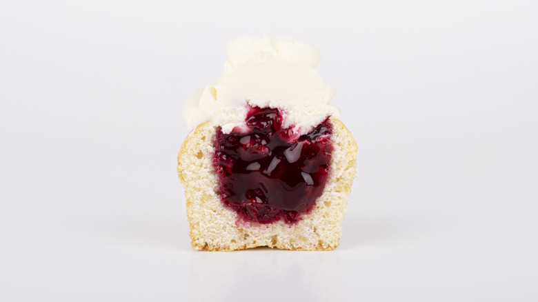 Vanilla cupcake with white frosting cut in half with jelly filling