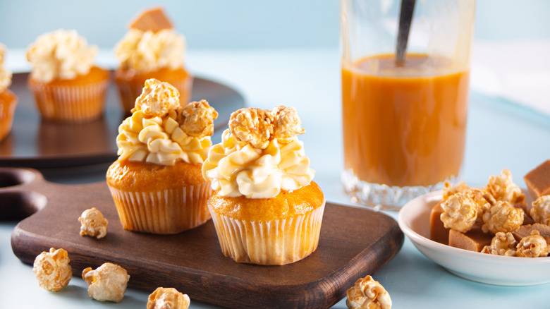 Vanilla cupcakes with white frosting and a popcorn topping on a wooden cutting board
