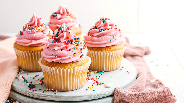 Vanilla cupcakes with pink frosting and sprinkles on a white platter
