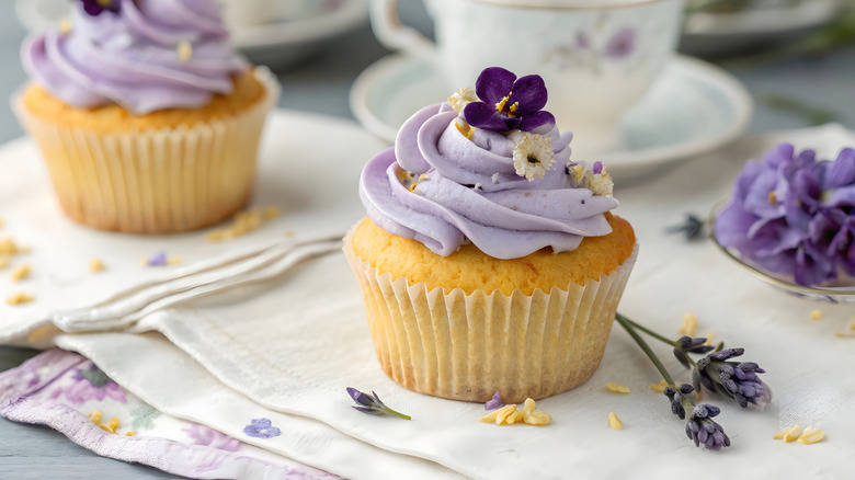 Vanilla cupcakes with purple frosting topped with edible flowers