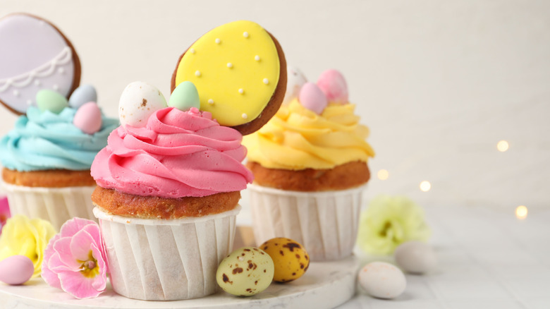 Vanilla cupcakes with different colored frosting topped with candy eggs