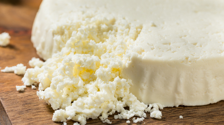Wheel of crumbly cotija cheese on wooden cutting board