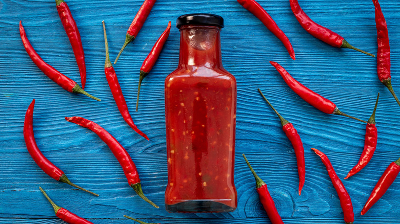 A bottle of homemade hot sauce surrounded by chile peppers
