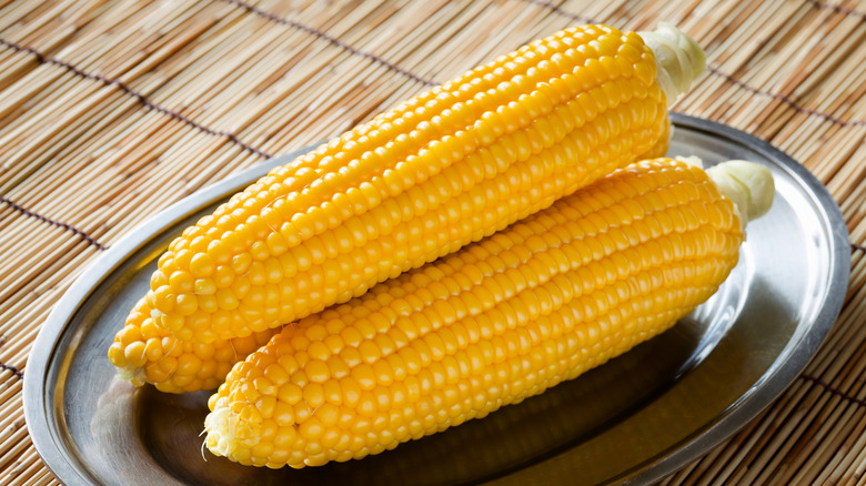Silver tray of three corn on the cob on placemat