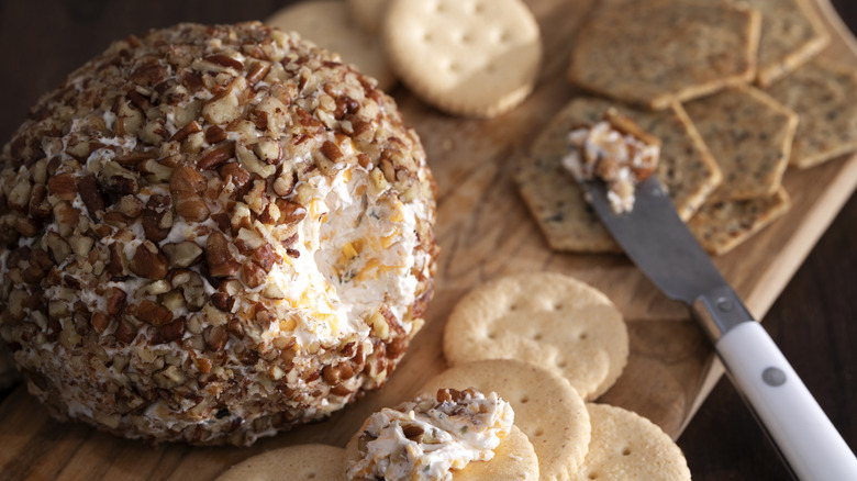 Close-up of a cheese ball covered in nuts on a cutting board with crackers.