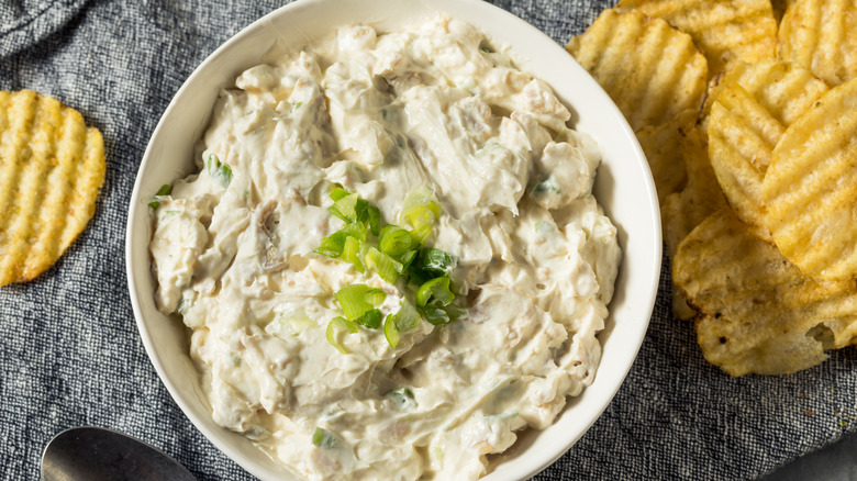 Bowl of claim dip surrounded by ridged potato chips.