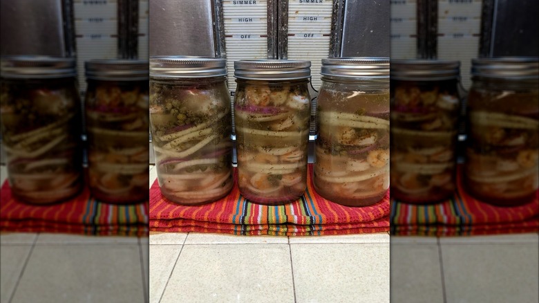 Three mason jars filled with pickled shrimp and aromatics.