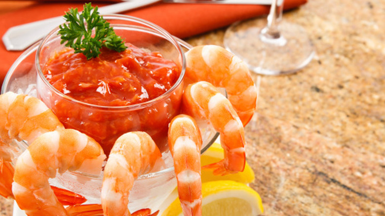 shrimp on ice in a cocktail glass surrounding a bowl of cocktail sauce
