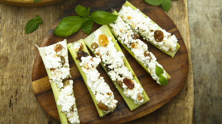 Celery stalks stuffed with cheese and raisins on a wooden serving platter.