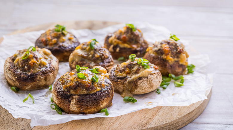 Stuffed mushroom caps on a piece of parchment paper atop a wooden serving plater.