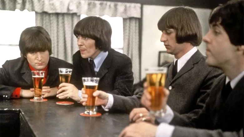 The four Beatles sit at a bar with their beers.